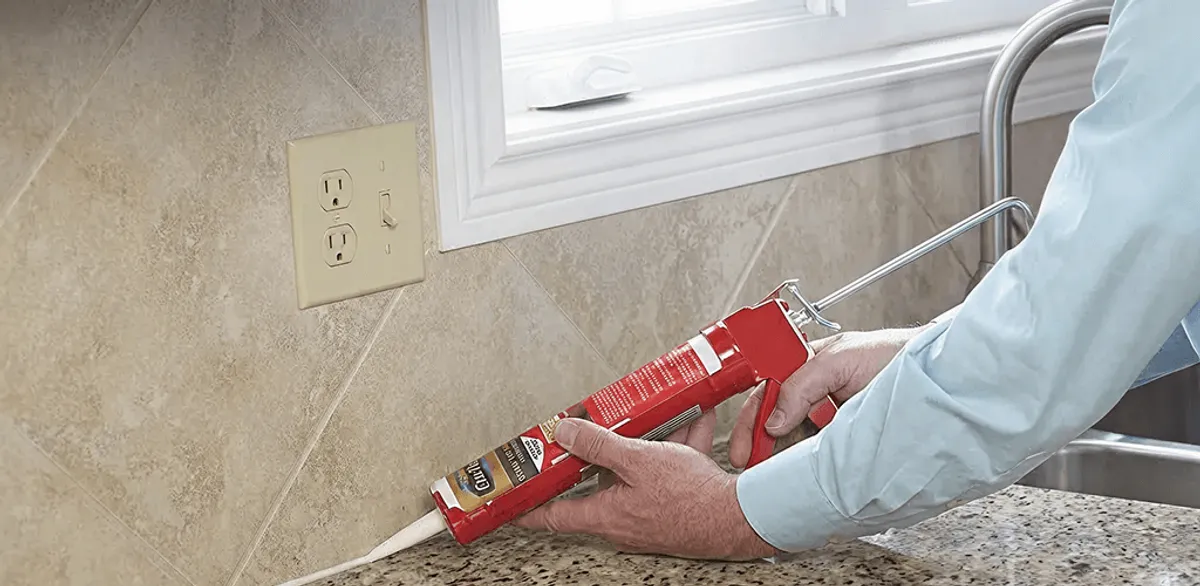 Handyman applying caulk along a kitchen backsplash and countertop seam in Marietta, GA