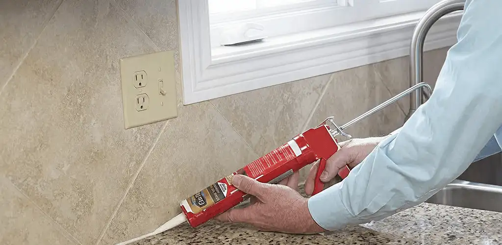 Handyman applying caulk along a kitchen backsplash and countertop seam in Marietta, GA
