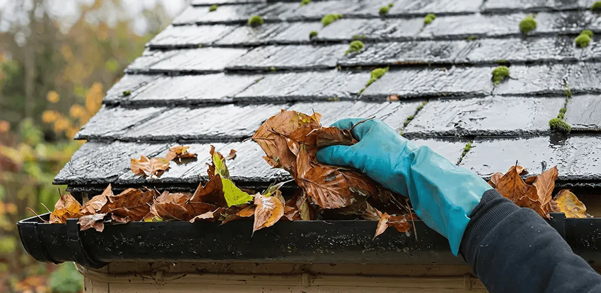 Gutter cleaning technician clearing wet leaves from roof gutters in Marietta, GA