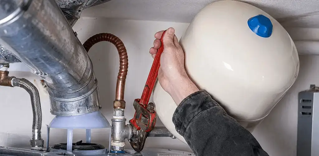 Water heater repair technician tightening plumbing connections near a tank unit in Marietta, GA